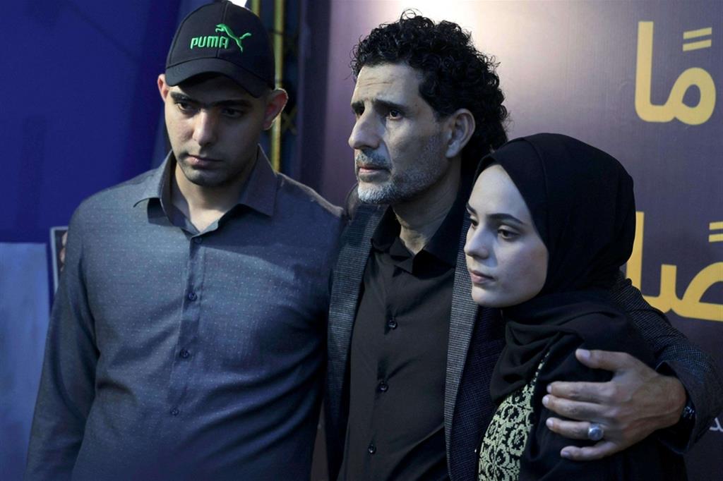 L'artista palestinese Zainab al-Qolaq, 22 anni, con il padre (al centro) e il fratello all'inaugurazione della mostra, il 24 maggio a Gaza, intitolata "Ho 22 anni e ho perso 22 persone" - Ansa