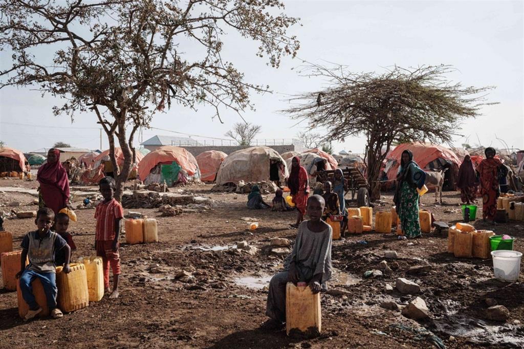 Alcune persone, tra cui diversi bambini, aspettano di riempire le proprie taniche d'acqua a Baidoa, in Somalia - Ansa
