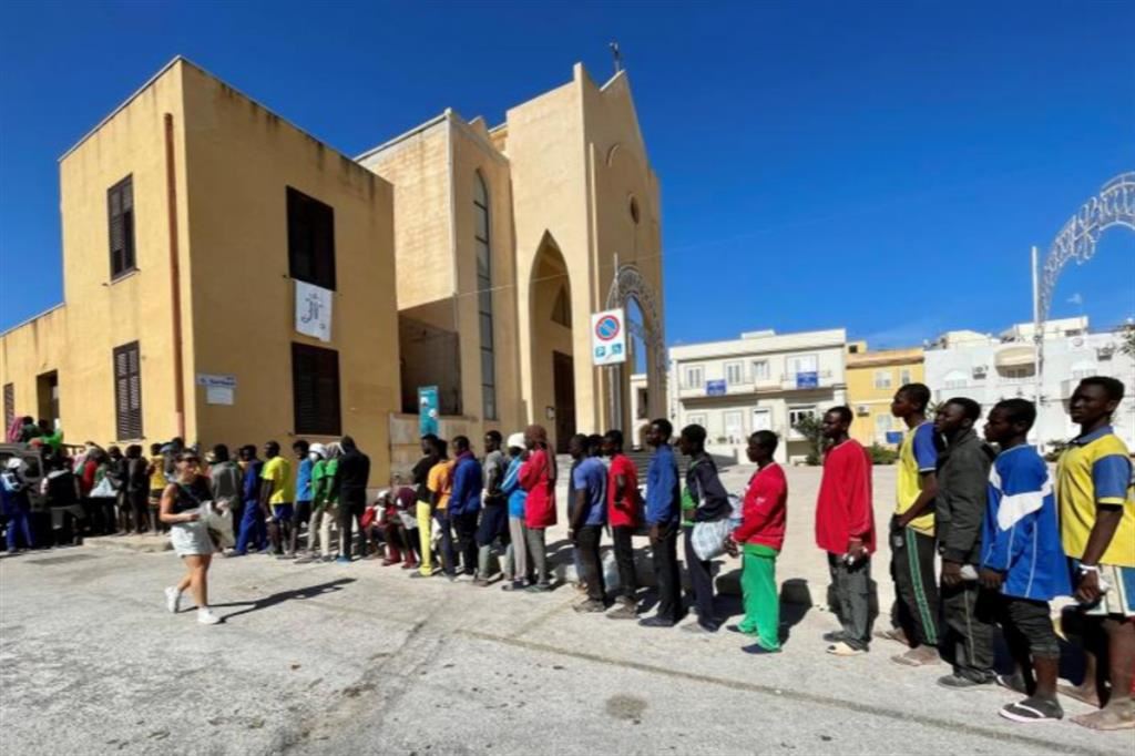 Migranti in coda davanti alla chiesa di San Gerlando a Lampedusa, Meloni ha bisogno di Saied, presidente della Tunisia, per bloccare i migranti (in qualsiasi modo)