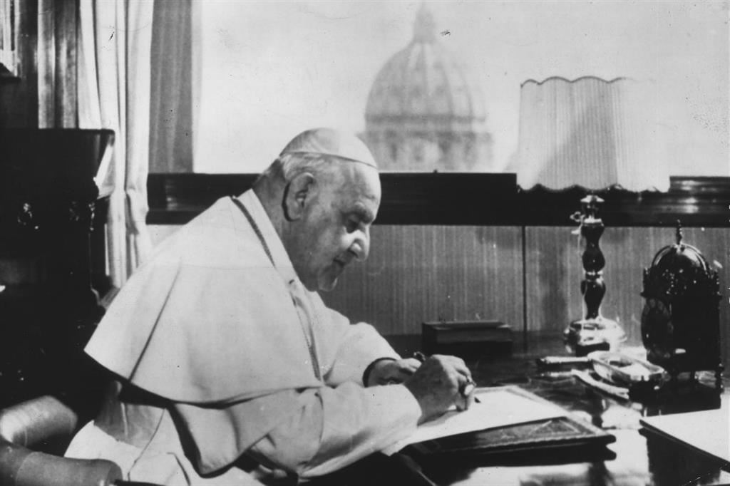 Giovanni XXIII al tavolo di lavoro nel suo studio. Sullo sfondo la cupola della Basilica di San Pietro