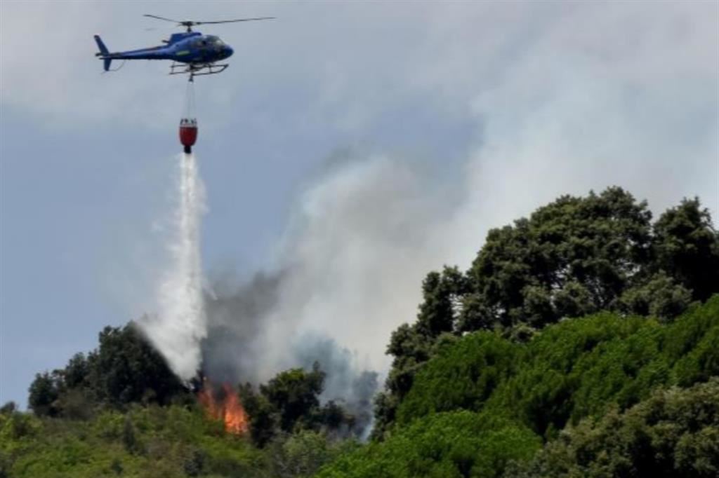 Un elicottero in azione contro le fiamme che stanno distruggendo un bosco