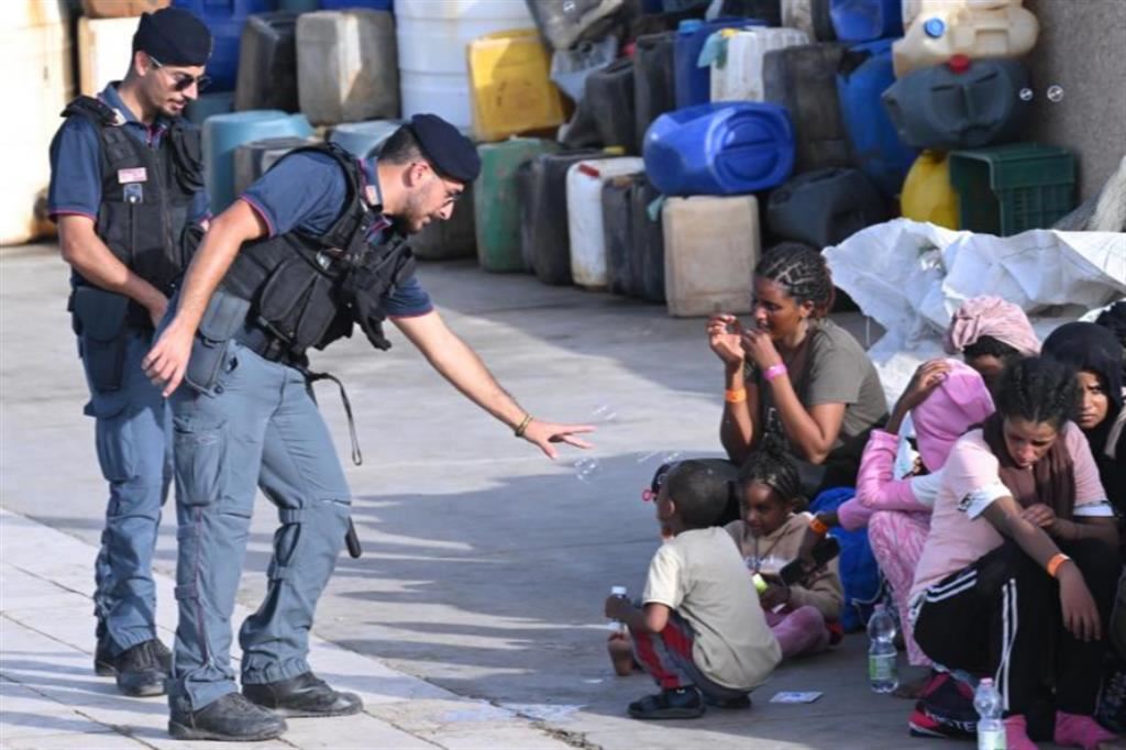 Un bambino gioca con un agente della Polizia con le bolle di sapone dopo l'arrivo nel porto di Lampedusa