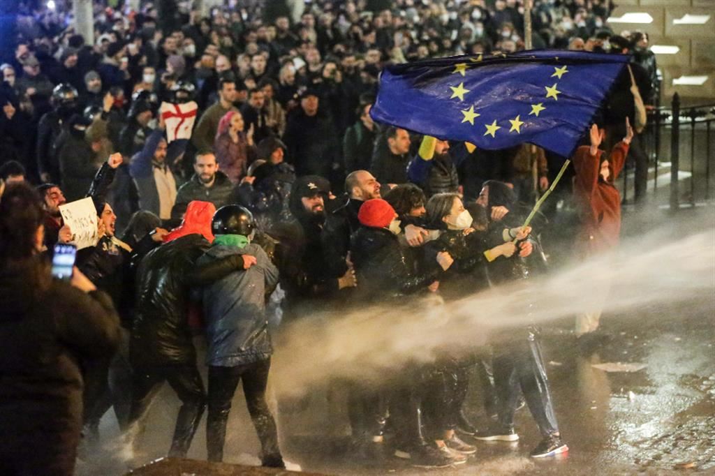 Una manifestante che sventola la bandiera dell'Unione Europea è investita dai getti degli idranti della polizia