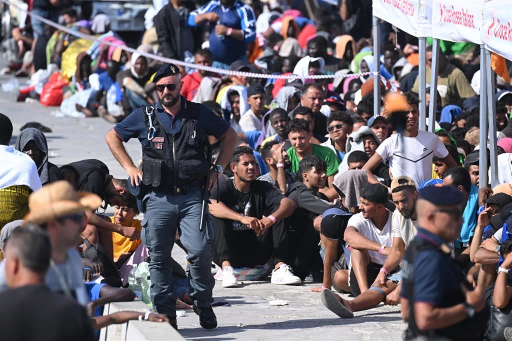 Migranti sulla banchina di Lampedusa in attesa di essere trasferiti
