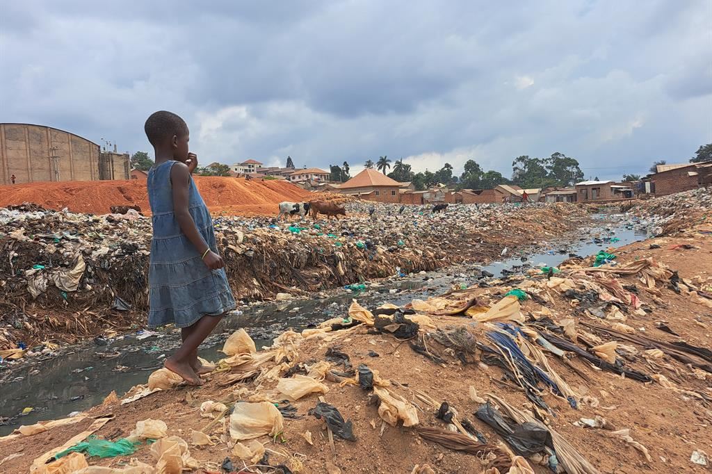 Una bambina vaga tra liquami e rifiuti nello slum di Katwe, a Kampala: molti bimbi vengono abbandonati nella capitale ugandese, dove sono preda di organizzazioni criminali