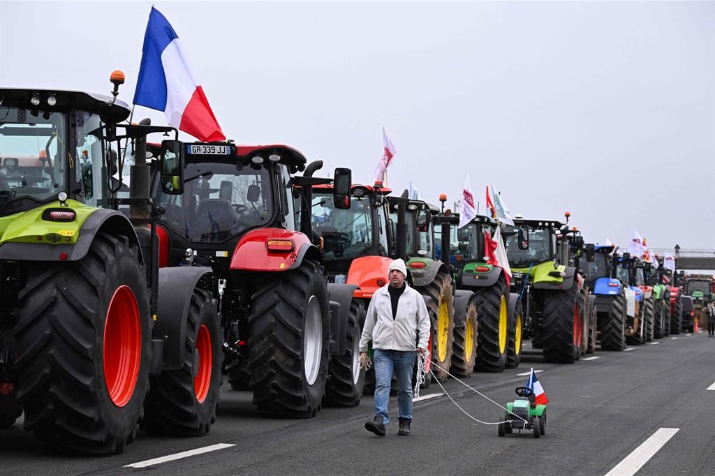Un agricoltore passa davanti ai trattori in fila trainando un trattore-giocattolo con la bandiera francese, durante una protesta che ha bloccato l'autostrada A4, vicino a Jossigny, a est di Parigi