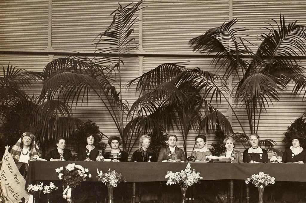 Al tavolo del Congresso delle donne di pace del 19154 al'Aja siede anche l'attivista italiana Rosa Genoni (nella foto, la prima a destra). "Tutte per una, una per tutte", recita lo striscione
